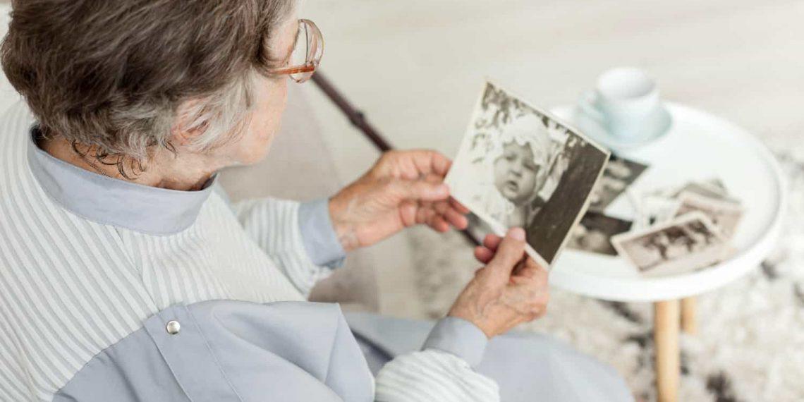 Senior woman looking thoughtful while holding a photo album, illustrating mom forgetting recent events