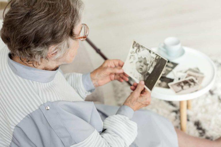 Senior woman looking thoughtful while holding a photo album, illustrating mom forgetting recent events