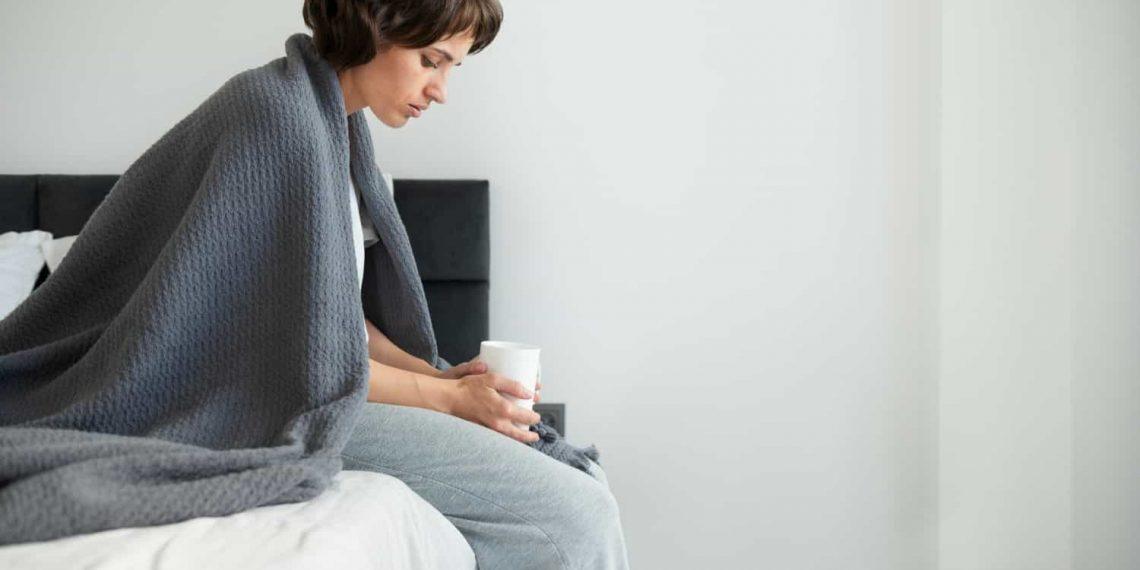 person sitting on edge of bed, experiencing symptoms of malaise