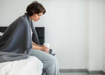 person sitting on edge of bed, experiencing symptoms of malaise