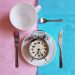 Clock on a plate with cutlery, concept of time management and meal planning.