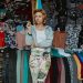 Woman in a clothing market surrounded by colorful garments.