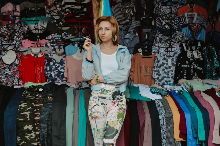 Woman in a clothing market surrounded by colorful garments.