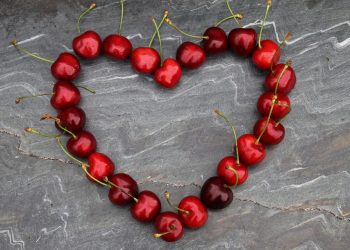 Red cherries arranged in a heart shape on a stone background.