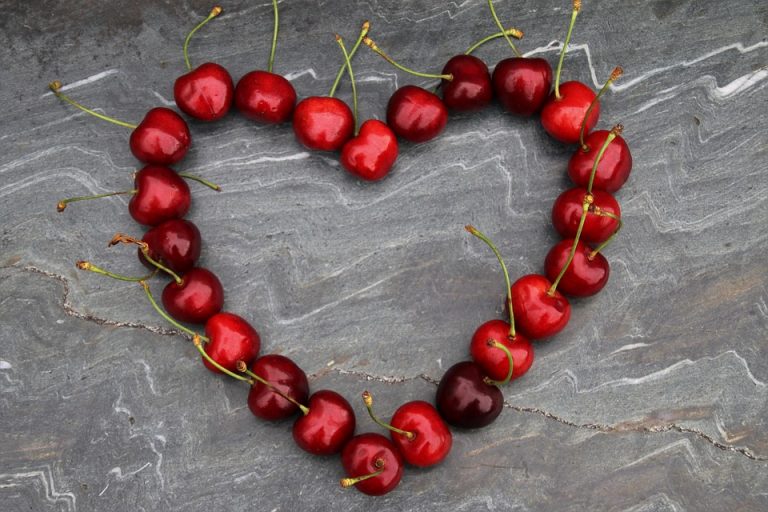 Red cherries arranged in a heart shape on a stone background.