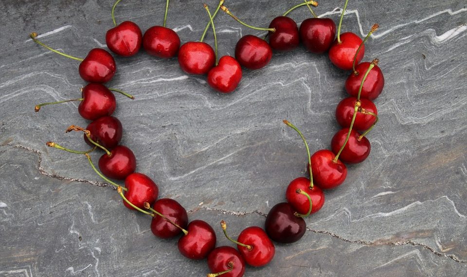 Red cherries arranged in a heart shape on a stone background.
