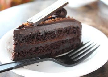 Chocolate layer cake slice on a white plate with a black fork.