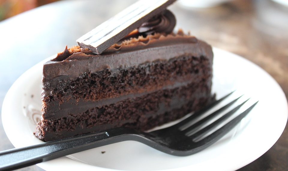 Chocolate layer cake slice on a white plate with a black fork.