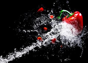 Red bell pepper splashed with water on black background.