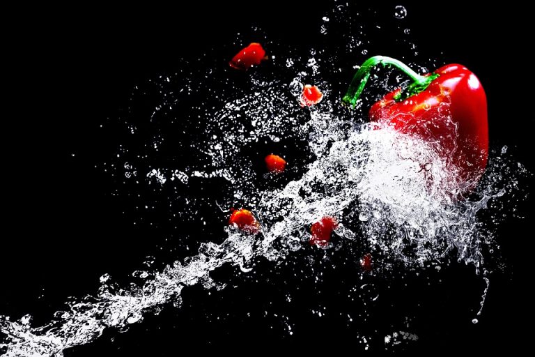 Red bell pepper splashed with water on black background.