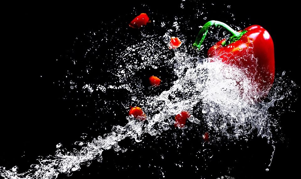 Red bell pepper splashed with water on black background.