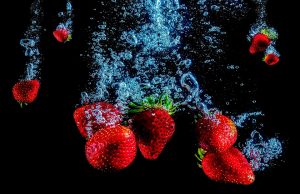 Strawberries splashing underwater against a dark background.