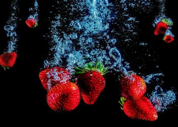 Strawberries splashing underwater against a dark background.
