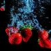 Strawberries splashing underwater against a dark background.