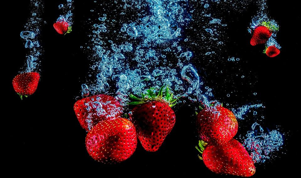 Strawberries splashing underwater against a dark background.