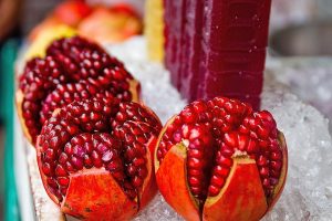 Pomegranate halves displayed on ice, with juice bottles behind.