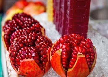 Pomegranate halves displayed on ice, with juice bottles behind.