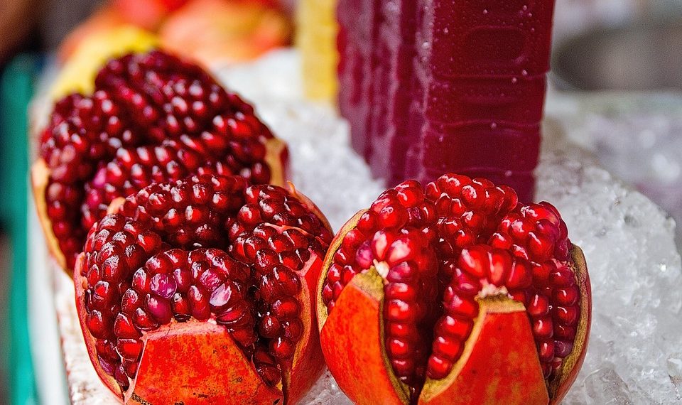 Pomegranate halves displayed on ice, with juice bottles behind.