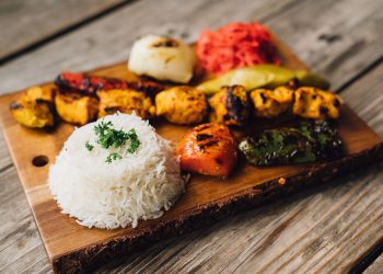 Grilled kebabs and rice served on a wooden platter.