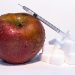 Apple with a syringe and sugar cubes representing the concept of food modification.