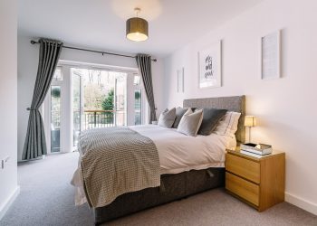 Modern bedroom with plush grey bed and open balcony doors.