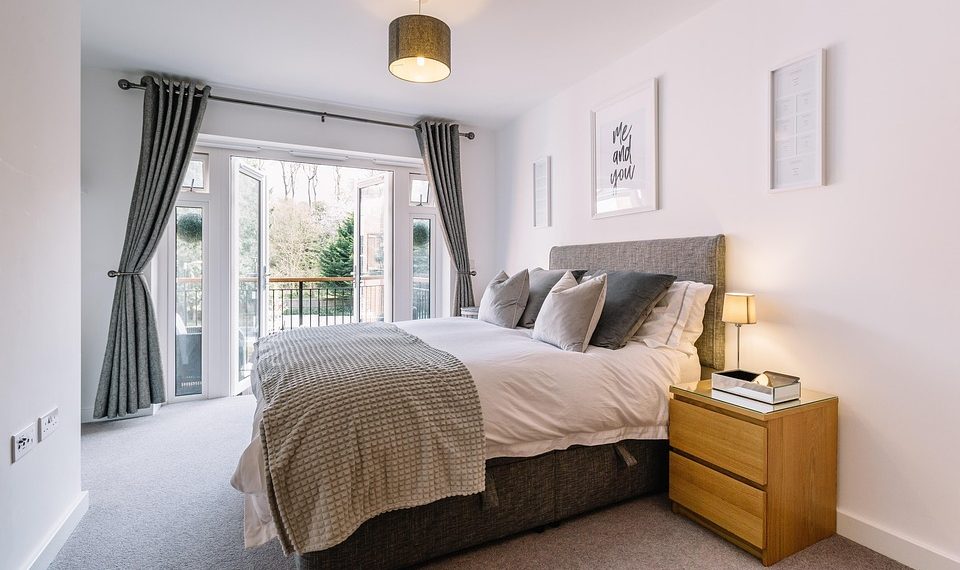 Modern bedroom with plush grey bed and open balcony doors.