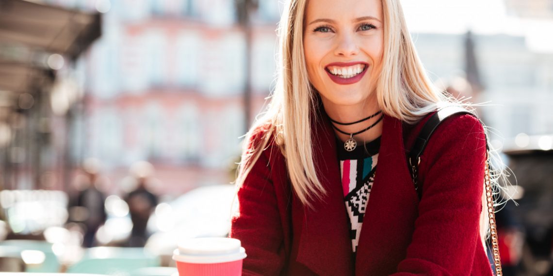 Smiling woman enjoying coffee outdoors.