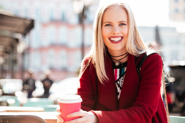 Smiling woman enjoying coffee outdoors.