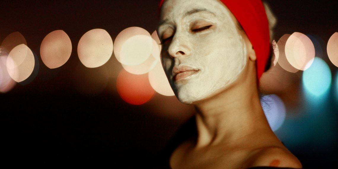 Woman with a face mask and red headband enjoying skincare.
