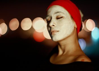 Woman with a face mask and red headband enjoying skincare.