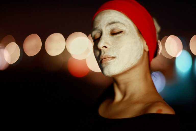 Woman with a face mask and red headband enjoying skincare.