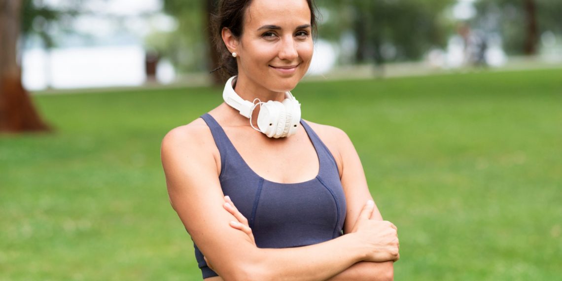 Woman with headphones smiling in a park.