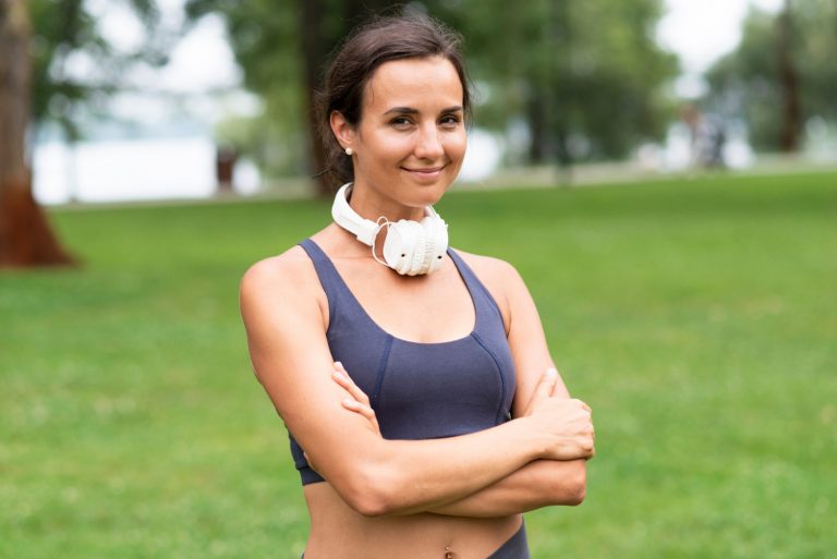 Woman with headphones smiling in a park.