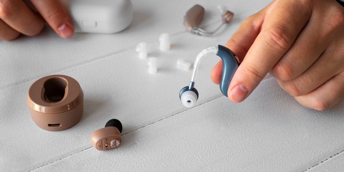 Hearing aid and wireless earbuds with accessories on a table.