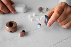 Hearing aid and wireless earbuds with accessories on a table.