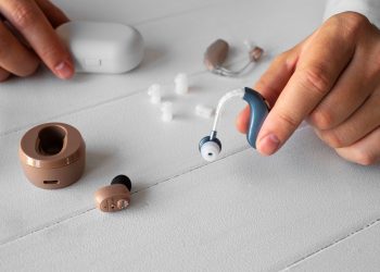 Hearing aid and wireless earbuds with accessories on a table.