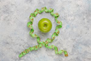 Green apple encircled by measuring tape on concrete background.