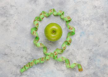 Green apple encircled by measuring tape on concrete background.