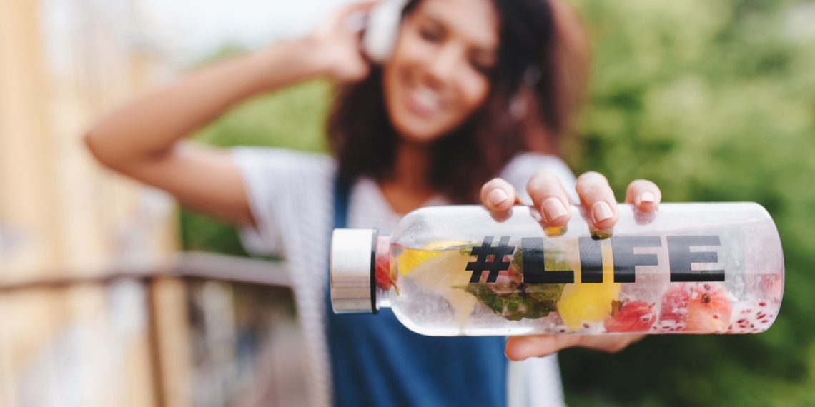 Young woman holding a fruit-infused water bottle labeled #Life.