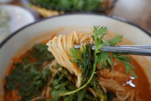 Chopsticks lifting spicy noodles with cilantro garnish.