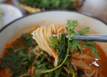 Chopsticks lifting spicy noodles with cilantro garnish.