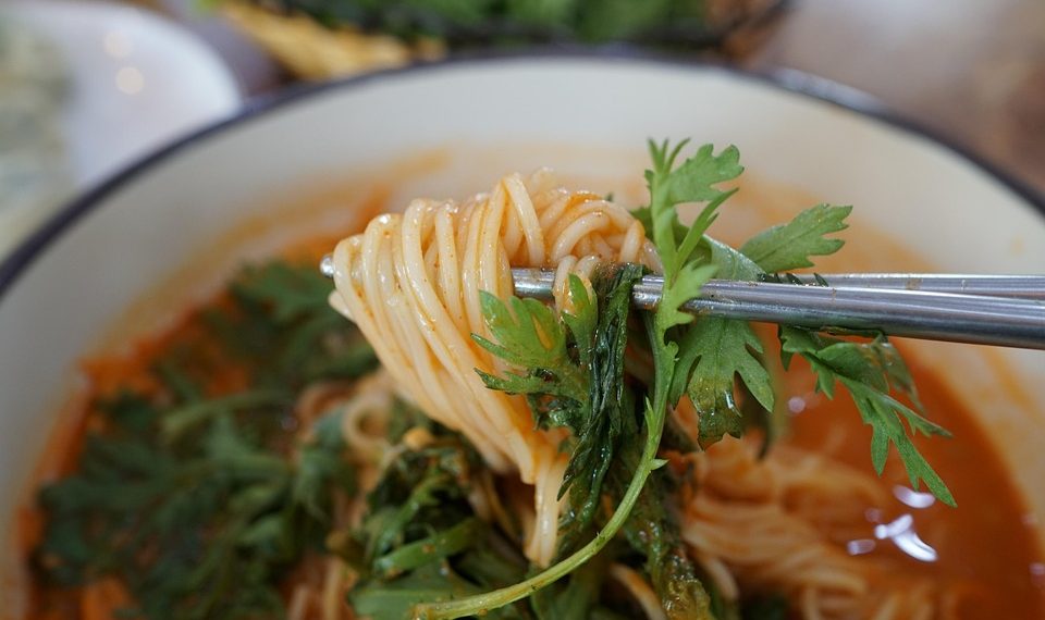 Chopsticks lifting spicy noodles with cilantro garnish.
