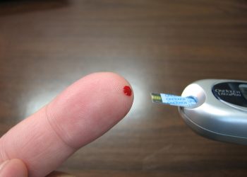Checking blood sugar with a glucose meter on fingertip.