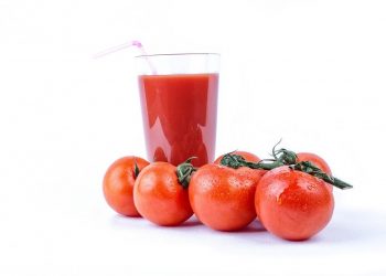Tomato juice in a glass surrounded by fresh tomatoes.