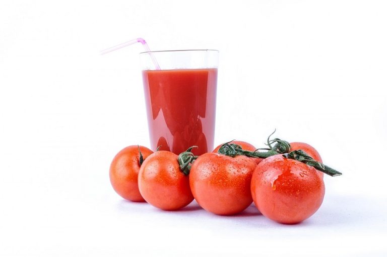 Tomato juice in a glass surrounded by fresh tomatoes.