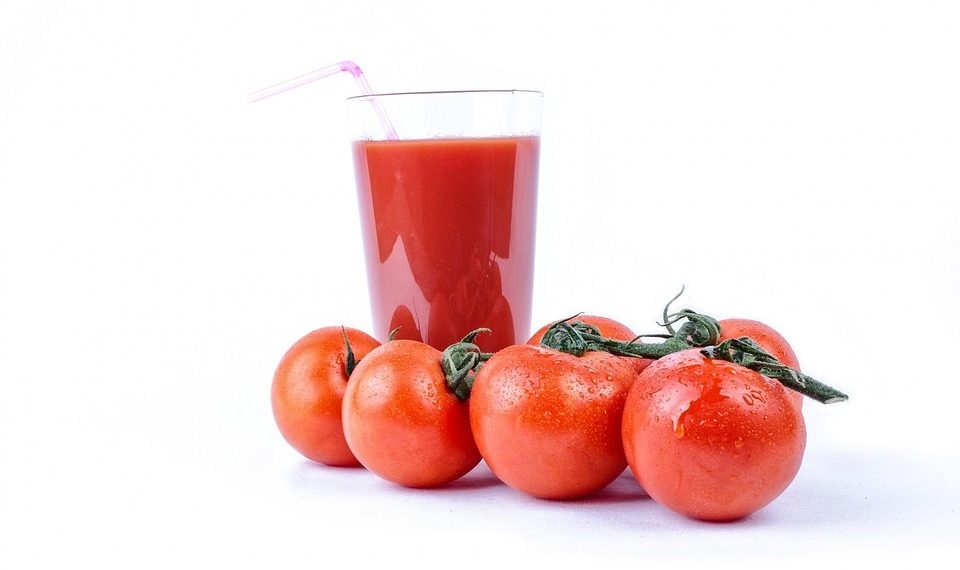 Tomato juice in a glass surrounded by fresh tomatoes.