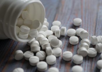 White pills spilled from a bottle on a wooden table.