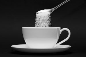 Pouring sugar from a spoon into a white cup.