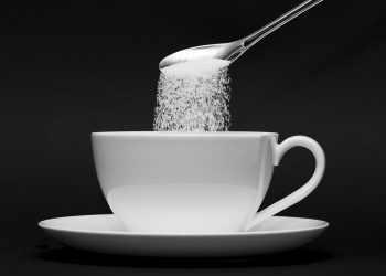 Pouring sugar from a spoon into a white cup.