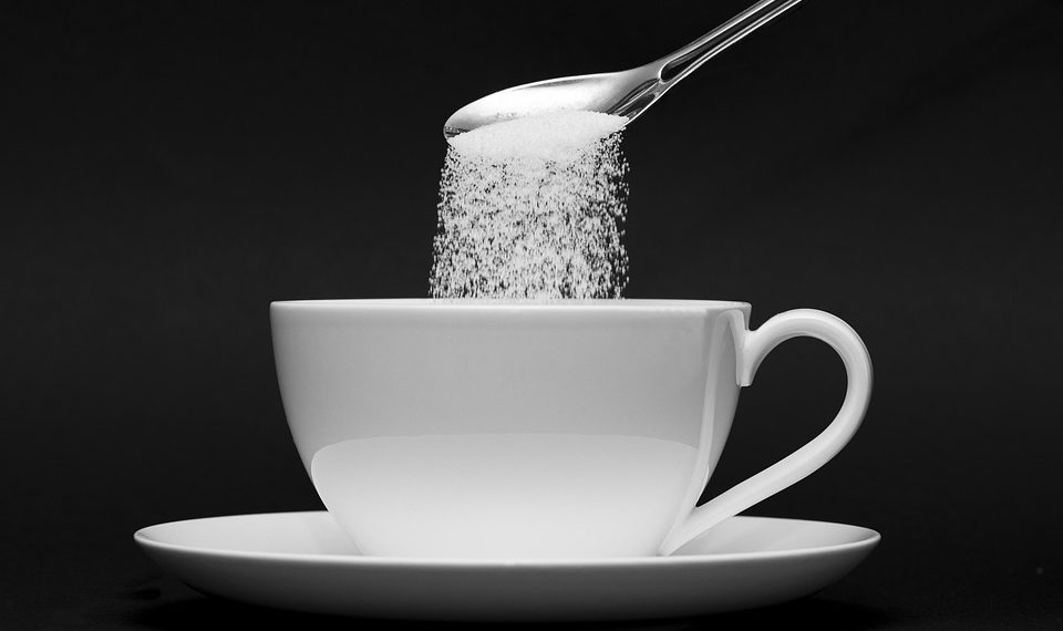 Pouring sugar from a spoon into a white cup.